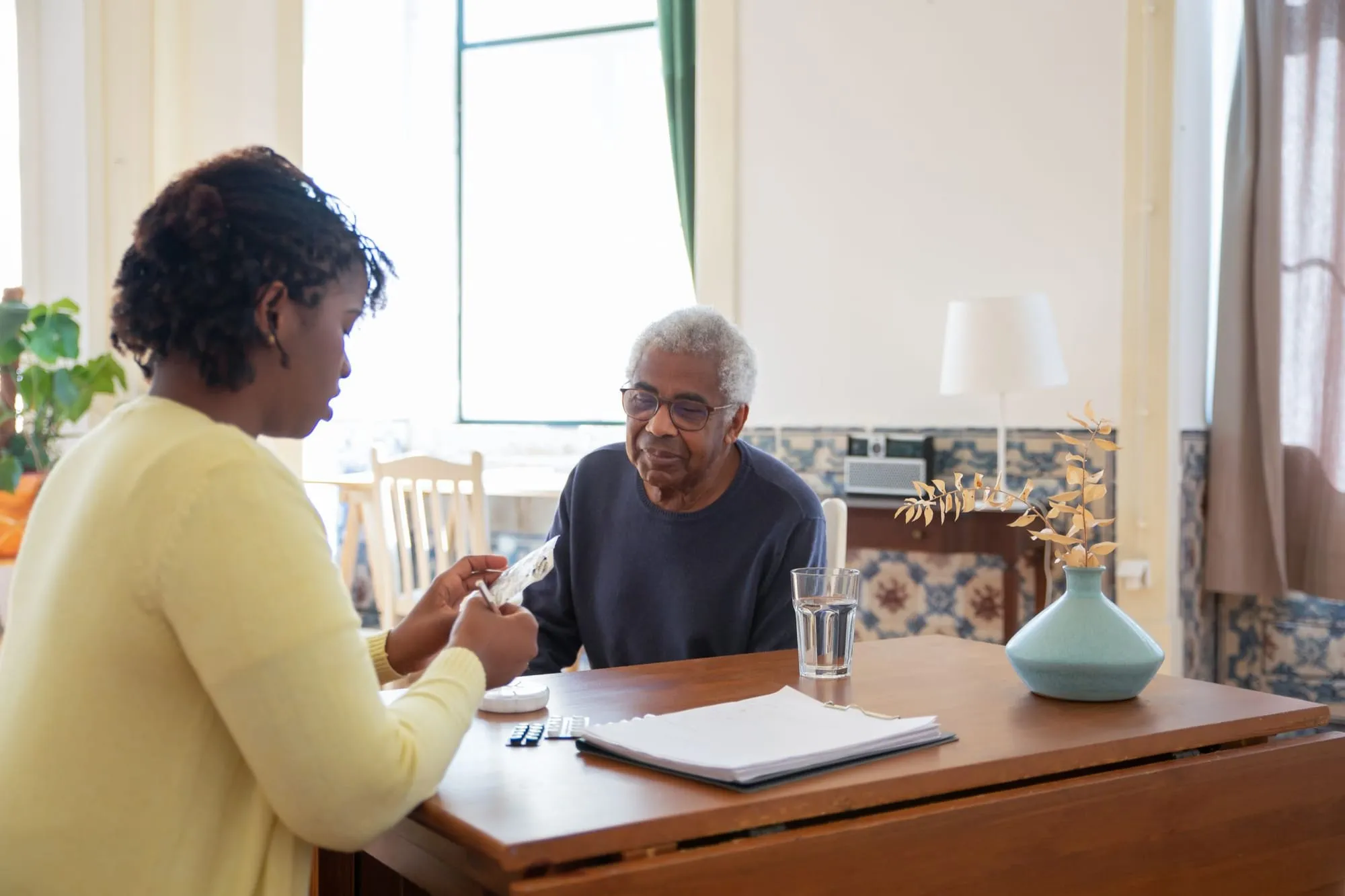 A caregiver sits at a table with an older man going over a paper together