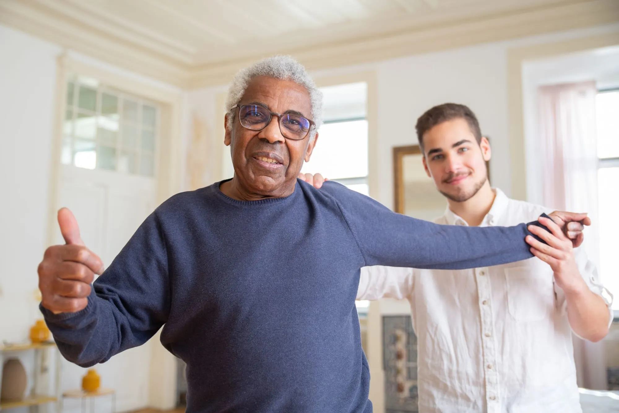 A cheerful older man gives a thumbs-up while a young man stands behind him