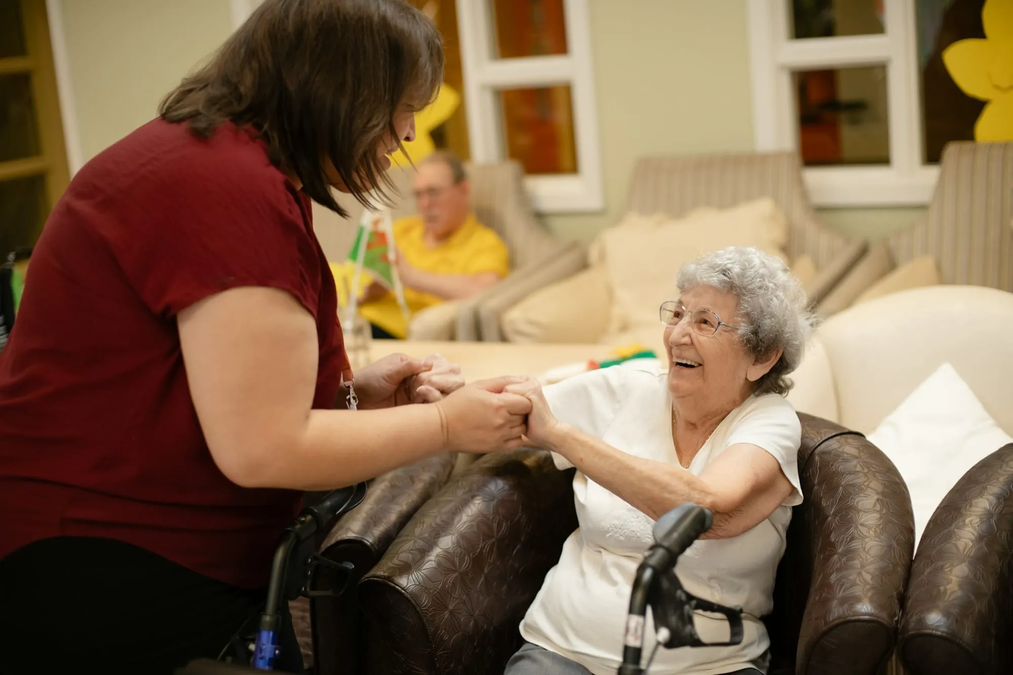 A caregiver holds the hands of a smiling older woman