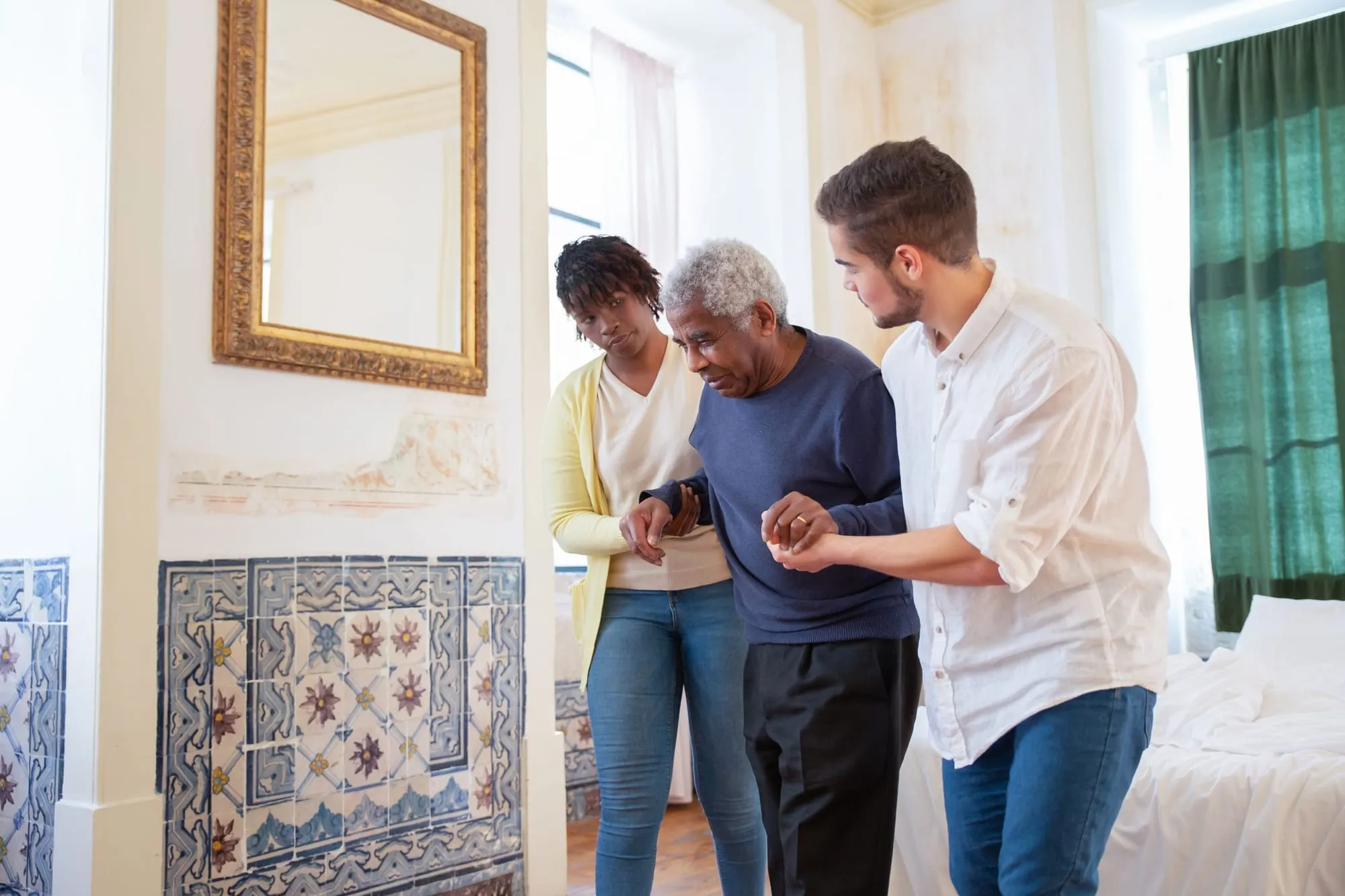 Two caregivers walk alongside an older man through his home
